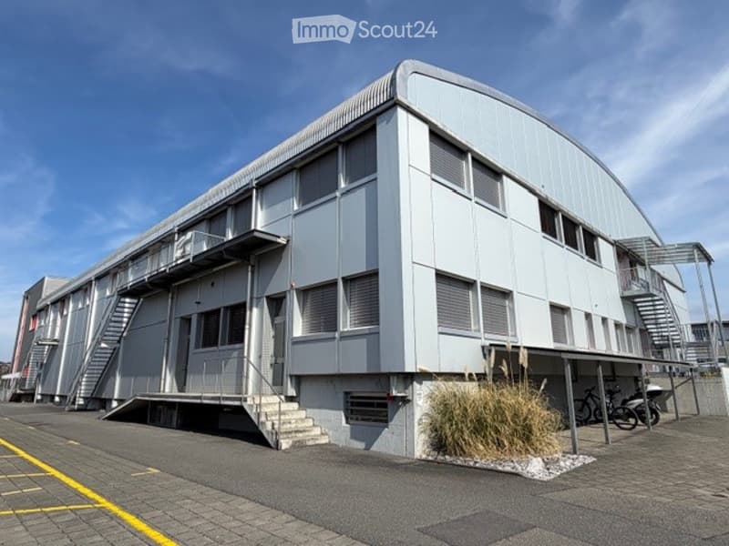 Industrial building, white exterior, multiple windows, stairs, parking area, bicycles parked