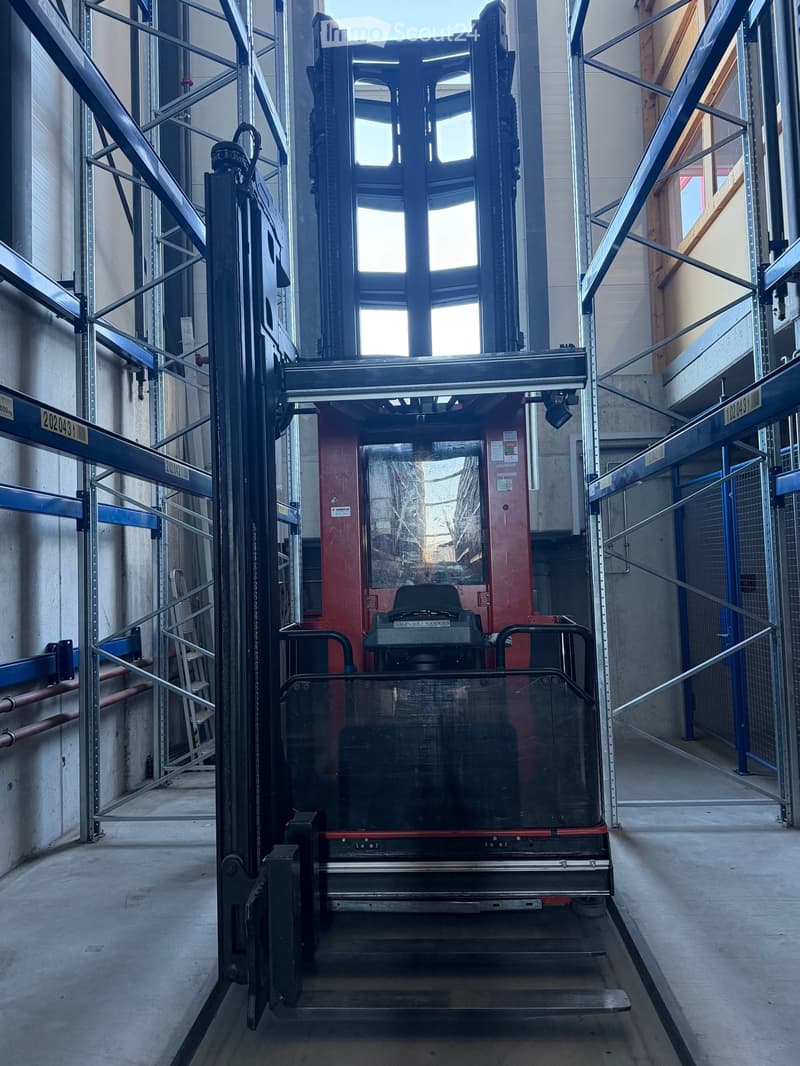 Industrial setting with a large forklift in the center, surrounded by metal shelving and storage units.