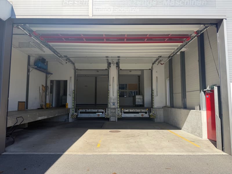 Empty garage with two loading docks, metal shelving, and a red door.