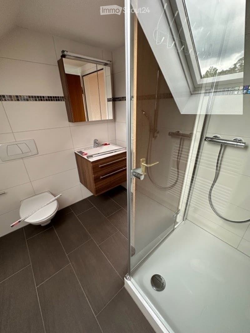 Bathroom with toilet, sink, shower, mirror, wooden cabinet, tiled floor, glass door, and window