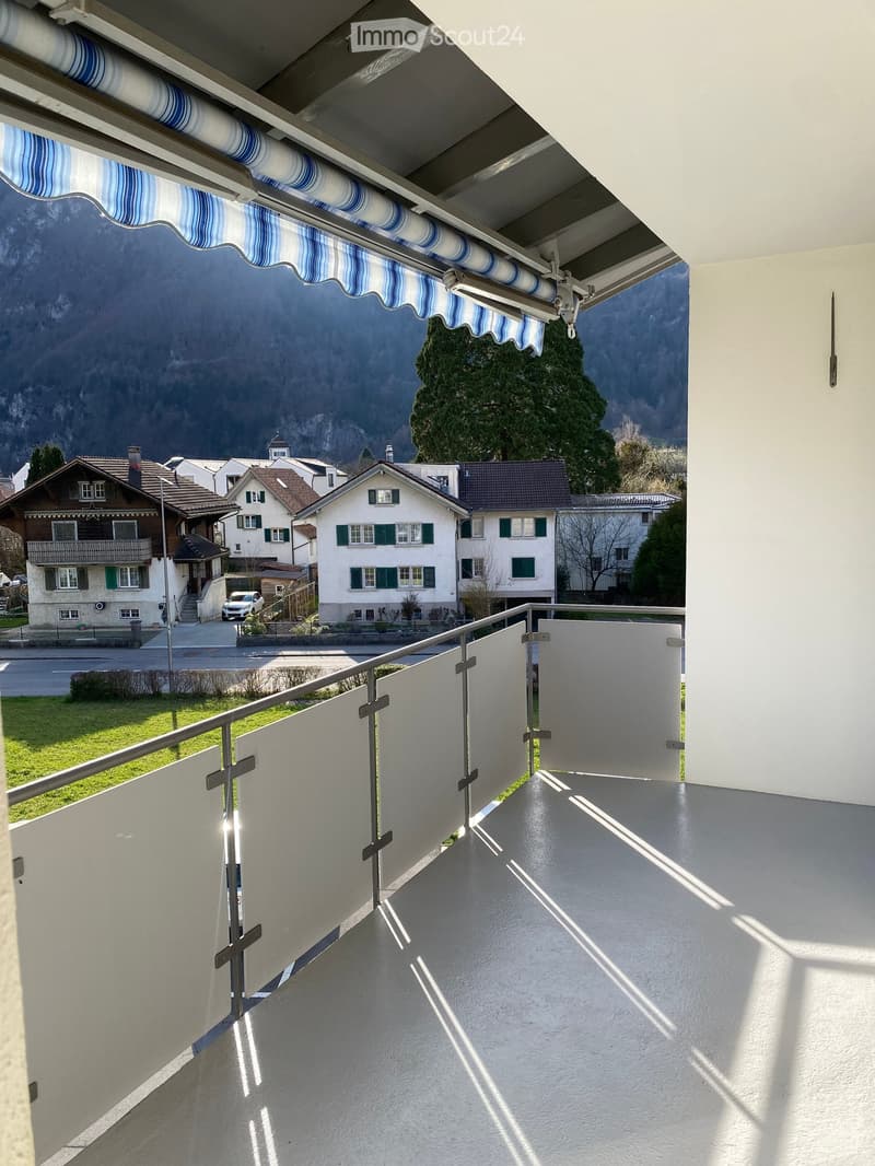 Balcony with metal railings, white floor, retractable awning, view of houses and mountains