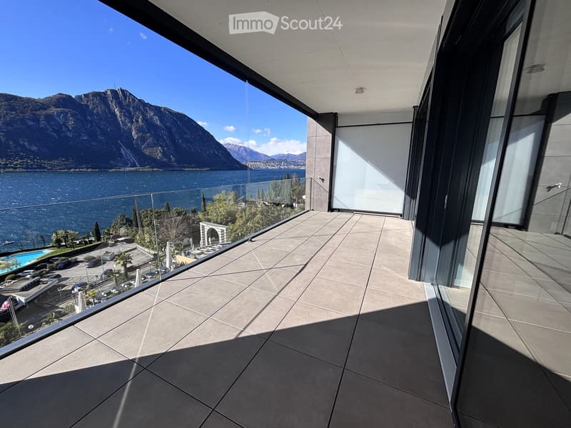 large balcony with glass railing, tiled floor, view of lake and mountains
