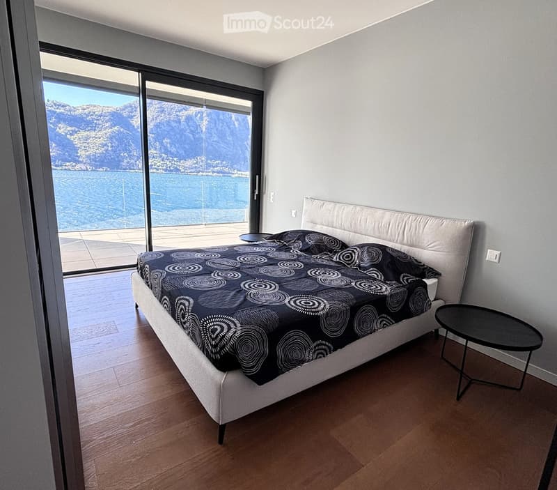 bedroom with large bed, bedside table, sliding glass doors, wooden floor, view of the lake