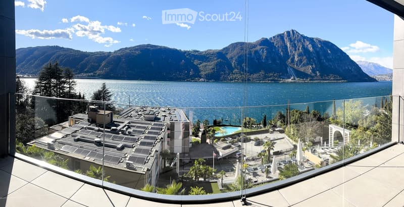 Building with glass balcony, solar panels on the roof, swimming pool, mountains, lake, and clear sky