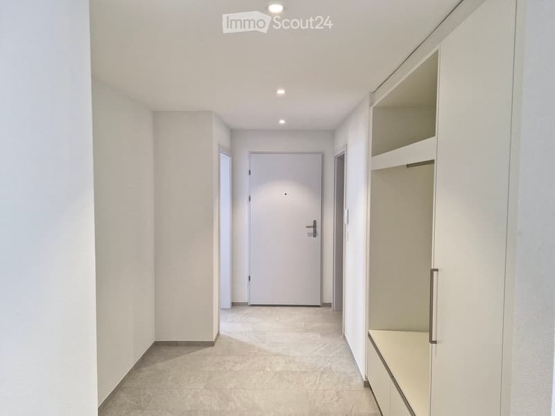 Empty hallway with white walls, tiled floor, white door, and built-in closets