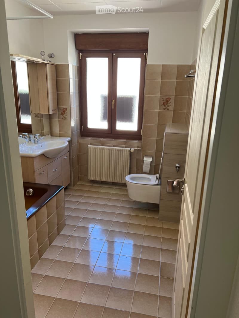 Bathroom with bathtub, sink, toilet, radiator, window, tiled floor, wooden cabinets, mirror