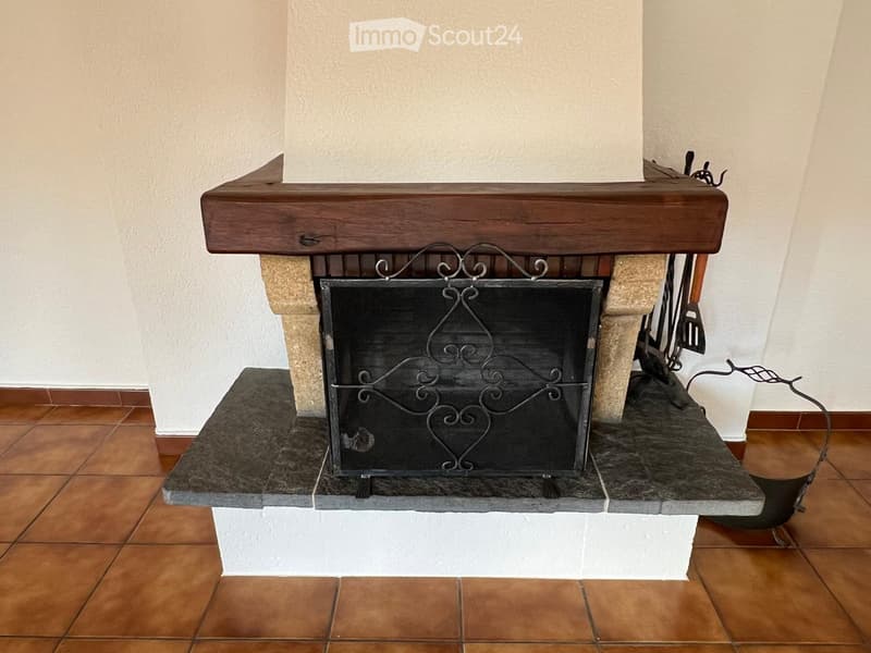Fireplace with wooden mantle, black metal grate, tiled floor, white walls