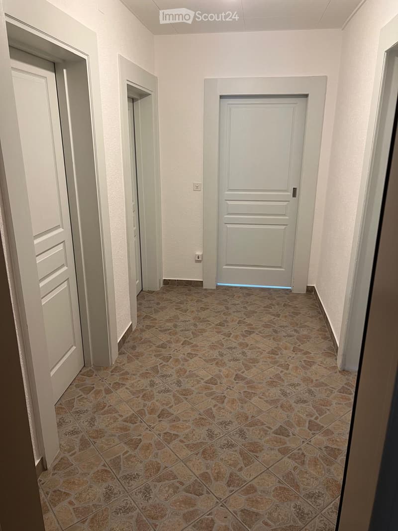 Empty hallway with tiled floor, white walls, three doors, and power outlets