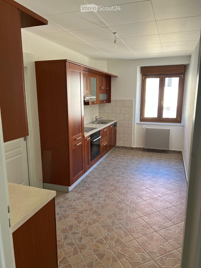 empty kitchen with wooden cabinets, tiled floor, sink, oven, window with radiator