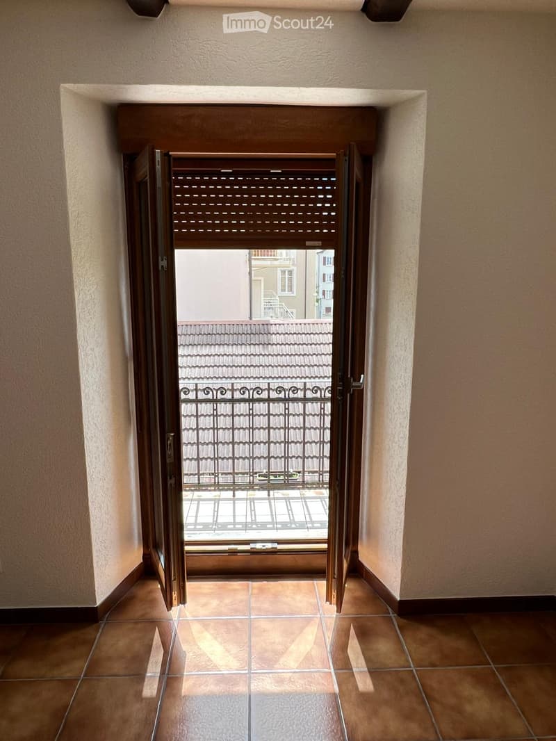 Open door leading to a balcony with a metal railing, tiled floor, white walls