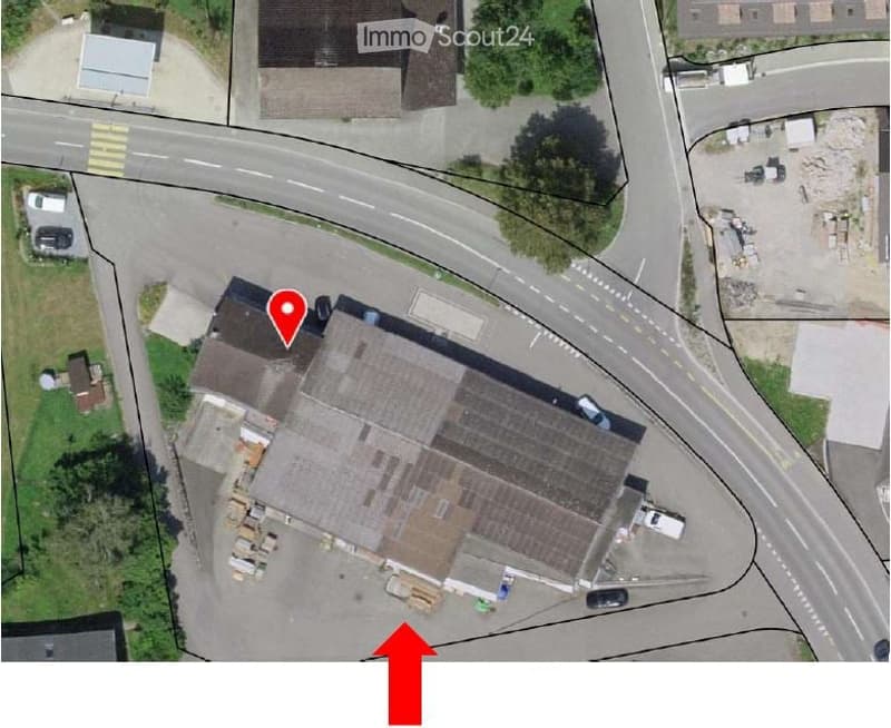 Warehouse building with a flat roof, located on a corner lot, surrounded by a parking lot, with several vehicles parked in front.