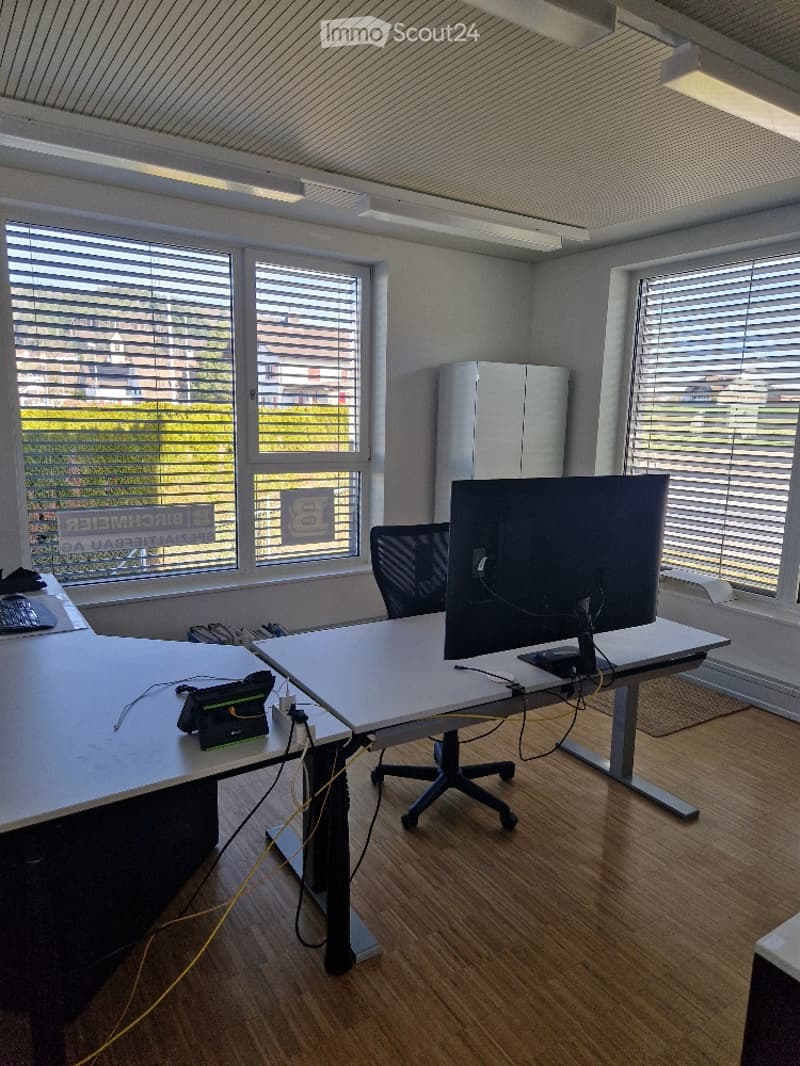 An office room with a desk, computer monitor, chair, and window blinds.