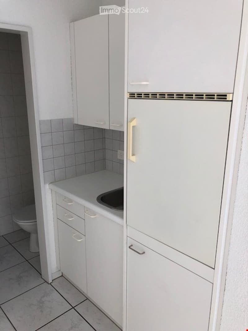 Small kitchen with white cabinets, tiled floor, sink, and refrigerator