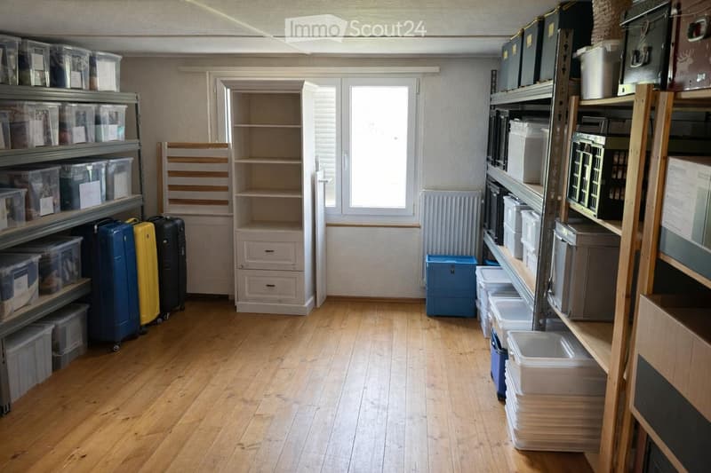 Storage room with wooden floor, white walls, shelves, storage boxes, suitcases, and a white radiator.