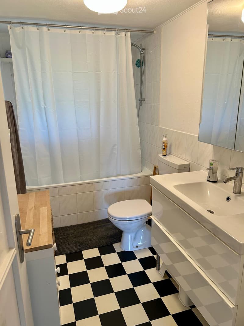 Bathroom with white tiles, black and white checkered floor, white bathtub, white toilet, white sink, mirror, and shower curtain.