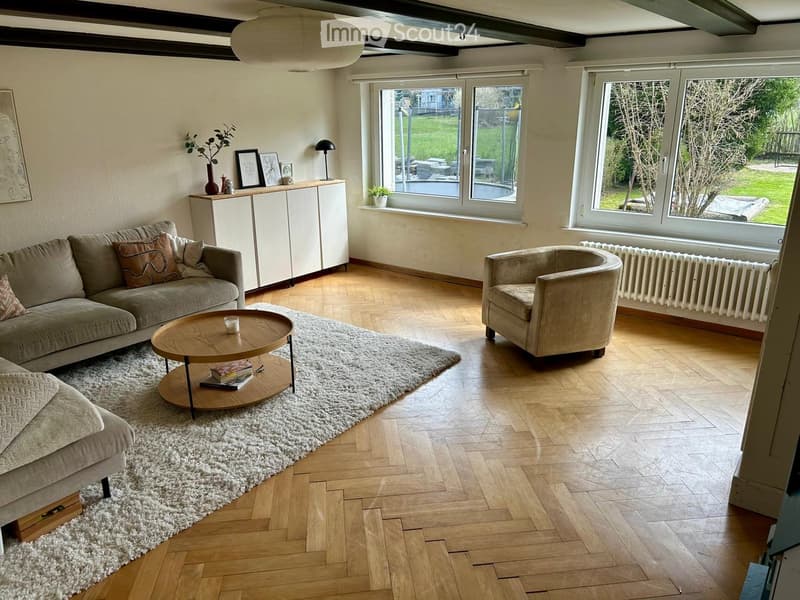 living room with wooden floor, couch, coffee table, armchair, white cabinet, radiator, windows, picture frame, plant, lamp