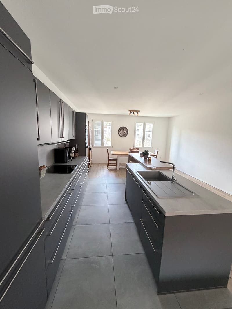 modern kitchen with gray cabinets, granite countertops, stainless steel sink, black appliances, tiled floor, dining area with table and chairs, large windows