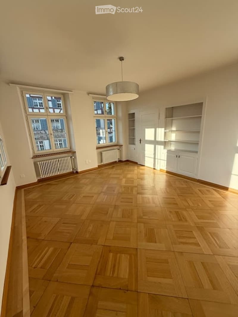 Empty room with wooden parquet flooring, white walls, large windows, ceiling lamp, built-in shelves, radiators