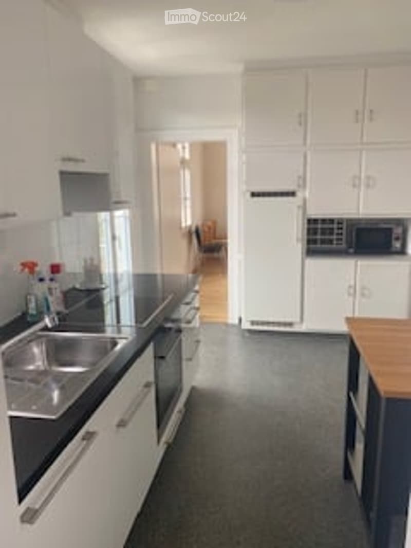 modern kitchen with white cabinets, black countertops, stainless steel sink, dishwasher, microwave, refrigerator, wooden table