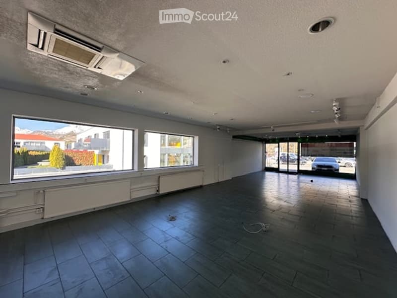 Empty room with large windows, tiled floor, white walls, and ceiling-mounted air conditioning units.