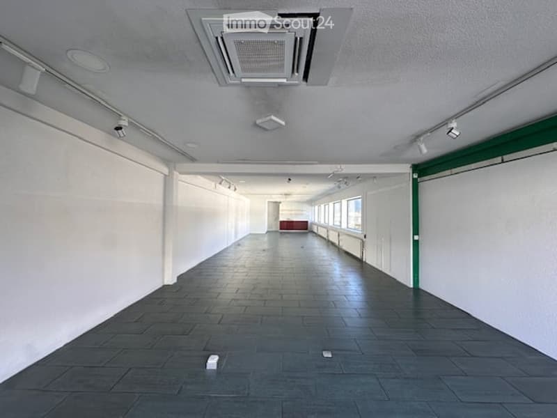 Empty room with white walls, black tiled floor, ceiling with air conditioning unit, track lighting, and windows