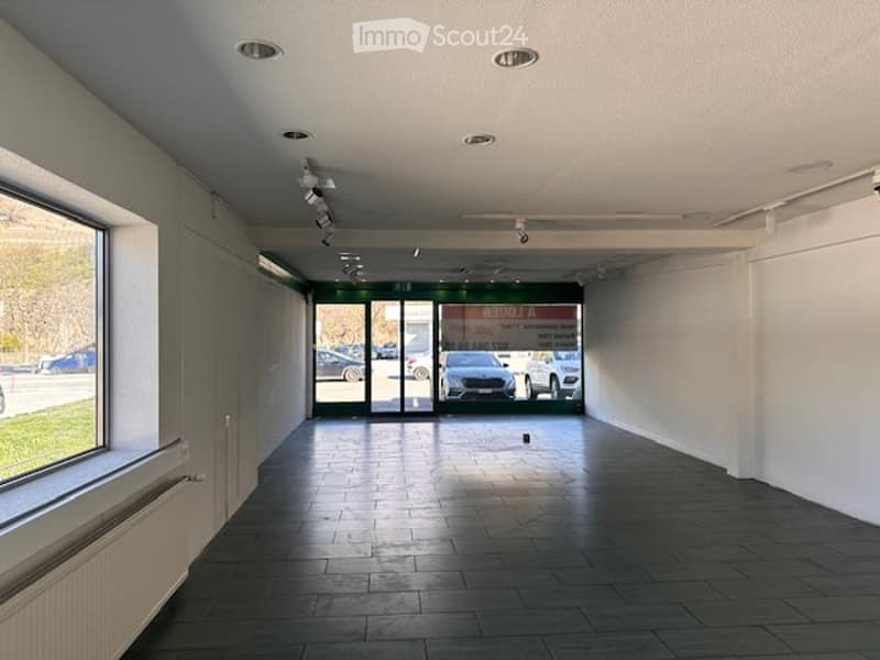 Empty room with white walls, black tiled floor, large window, radiator, ceiling lights, glass doors, and a signboard