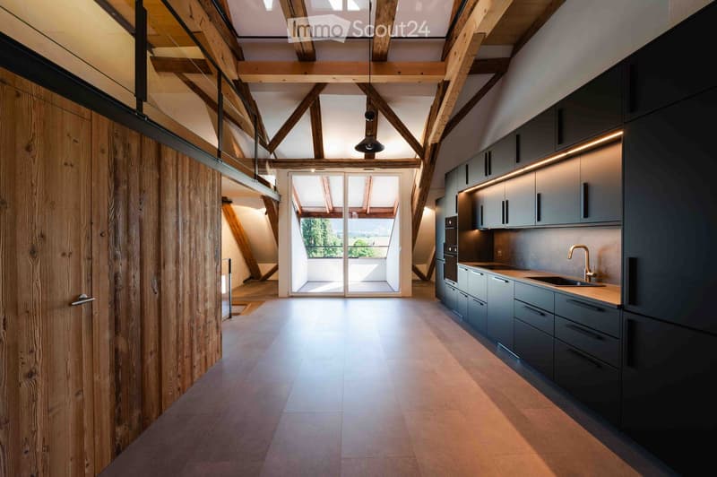 Modern kitchen with grey cabinets, stainless steel sink, and a view through large glass doors to an outdoor area.