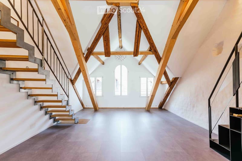 Bright, open hallway with wooden beams and a modern staircase leading upwards, featuring a sleek metal railing and wooden steps.