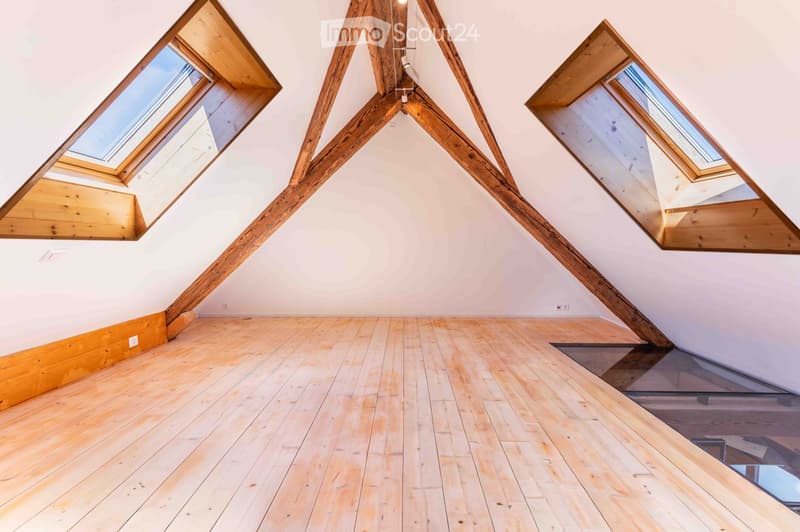 Empty attic space with wooden beams, skylights, and wooden flooring.