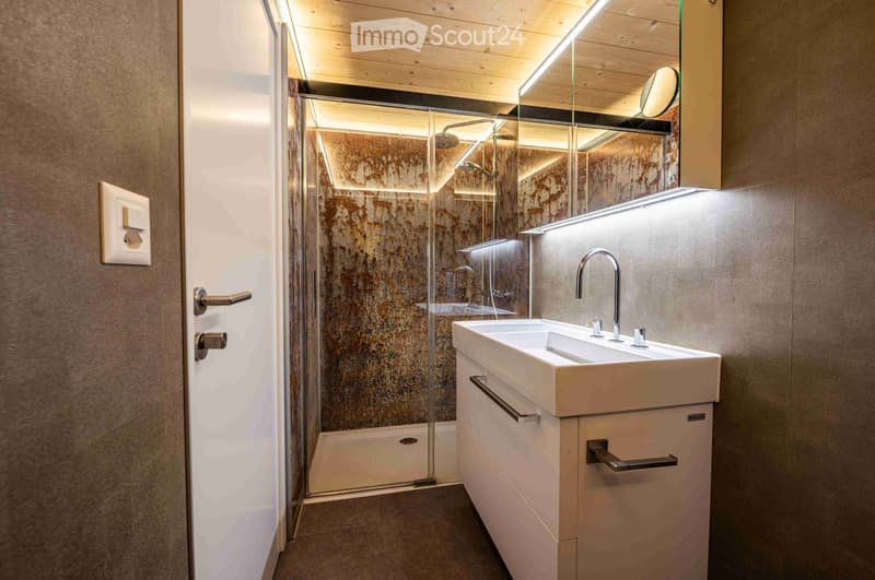 Modern bathroom with a white sink, sleek faucet, large mirror, and a glass-enclosed shower with a textured wall.