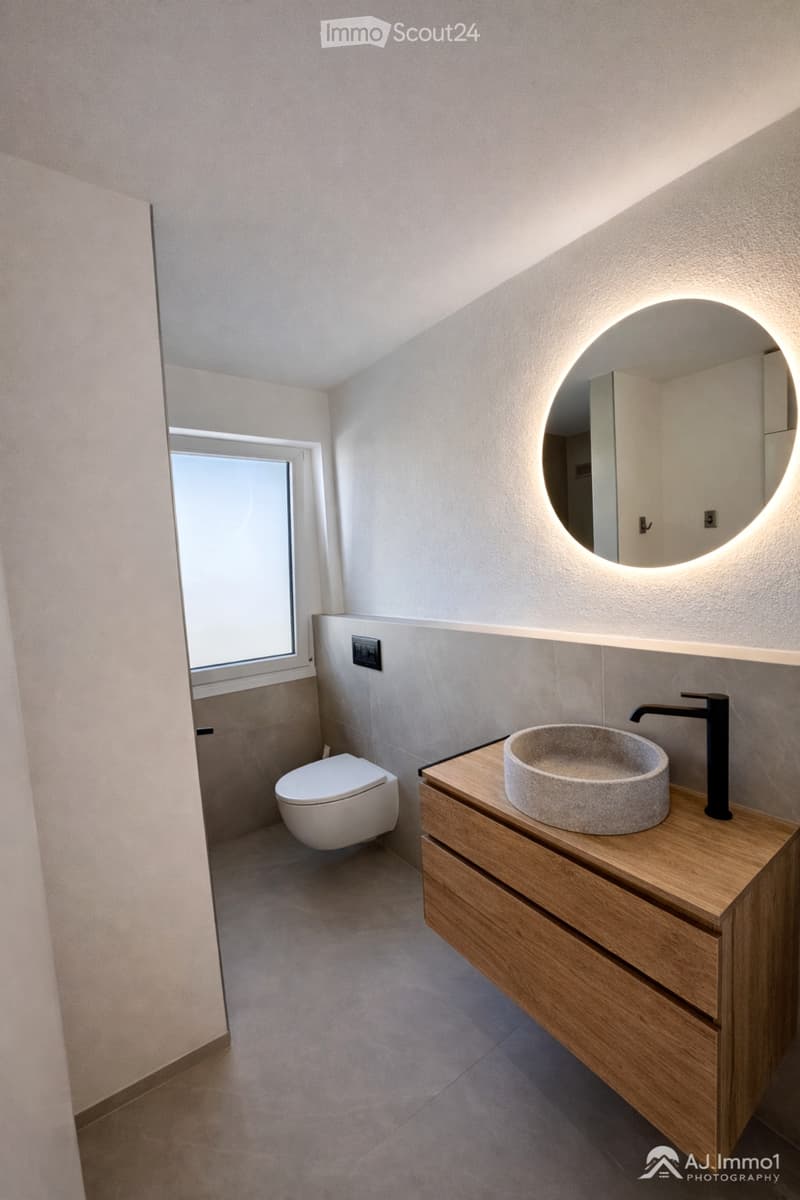 modern bathroom with white toilet, round mirror, wooden vanity, stone sink, black faucet