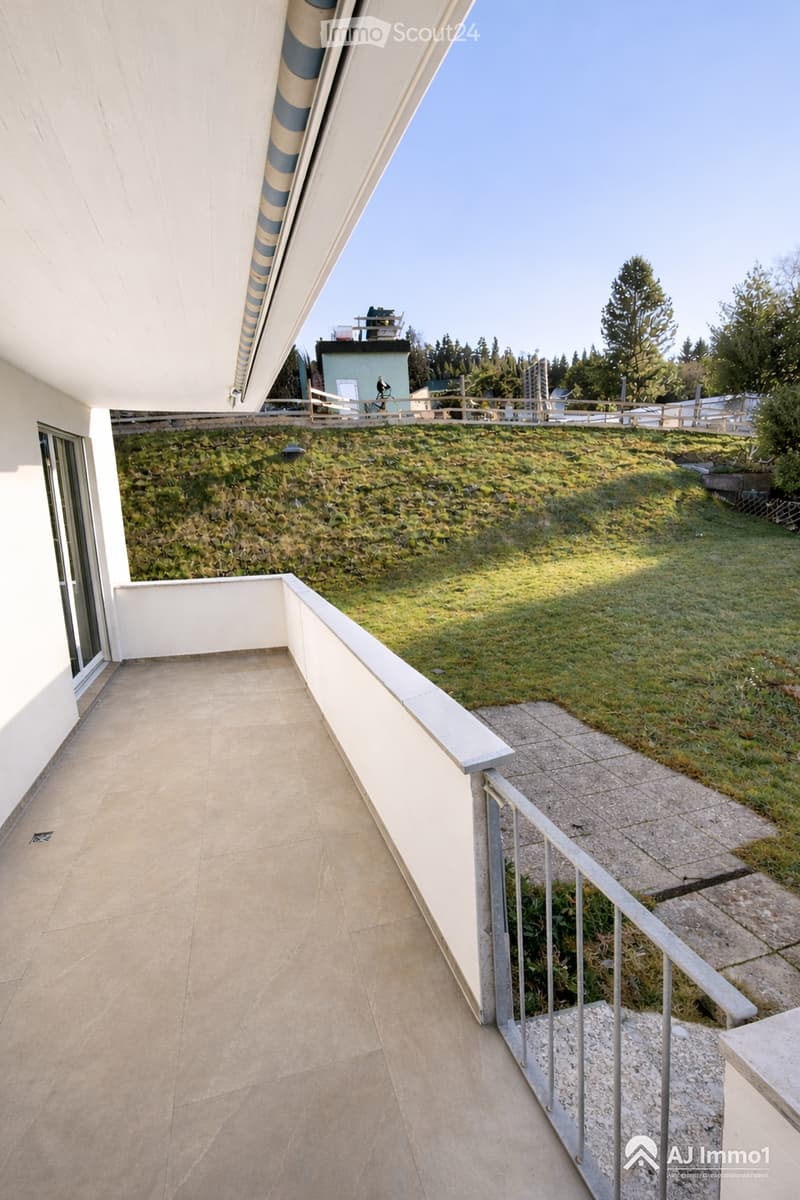 Balcony with tiled floor, metal railing, and a view of a grassy hill and trees