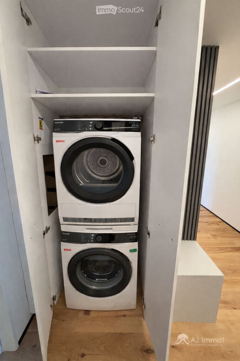 A white built-in wardrobe with shelves and a door that opens to reveal a stacked washer and dryer.
