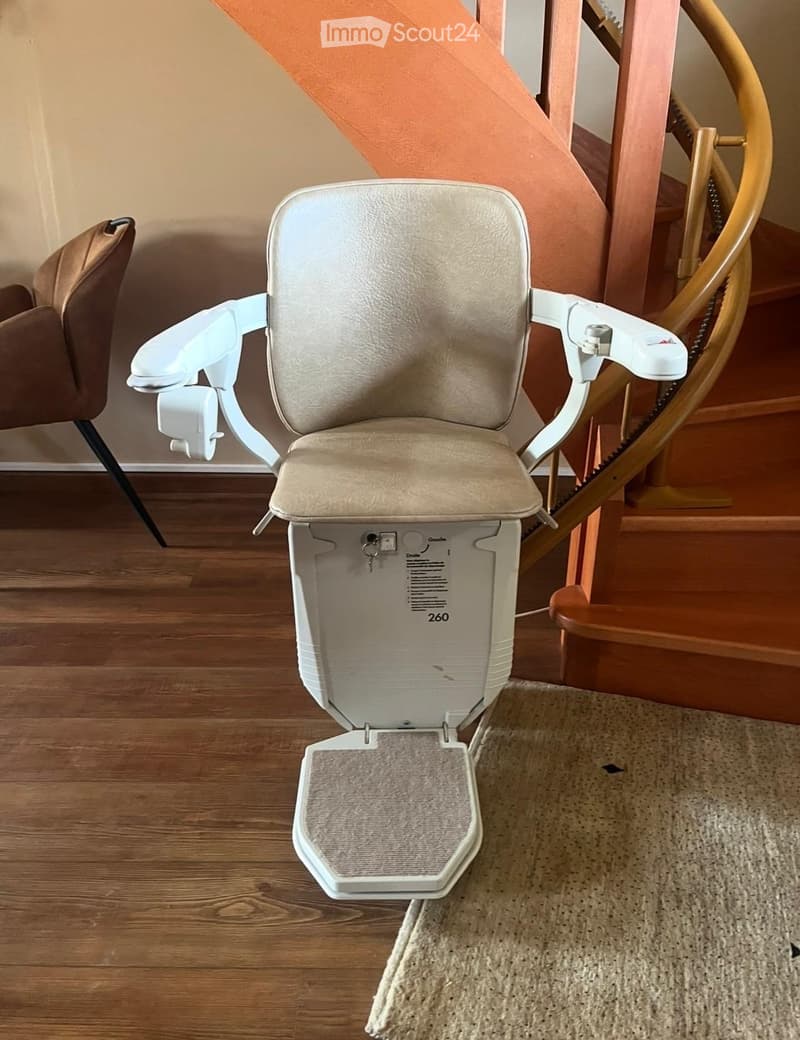White stairlift with beige seat, located in a room with wooden floor and spiral staircase