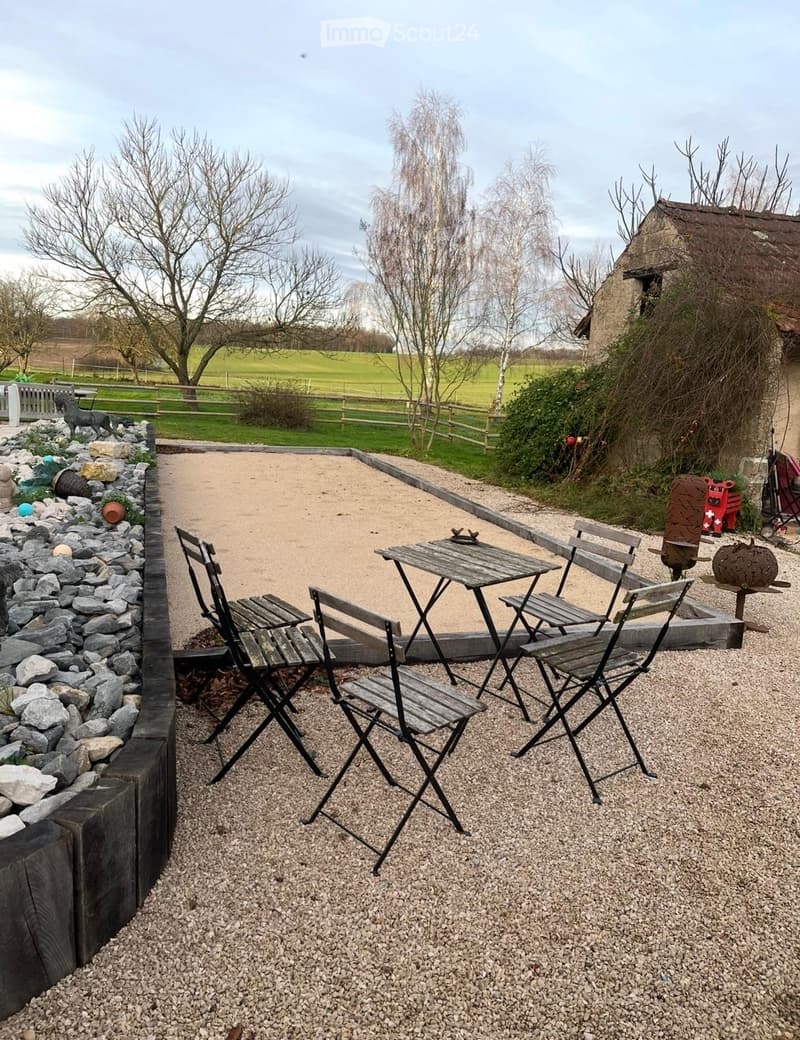 Outdoor area with a sand pit, wooden chairs, a small table, and a gravel path.