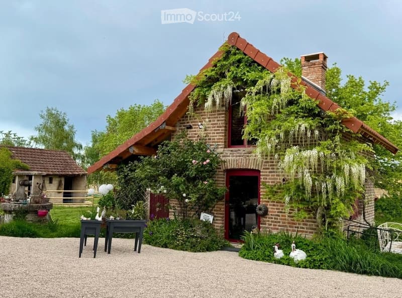 Small brick house, red roof, covered in greenery, garden, gravel driveway