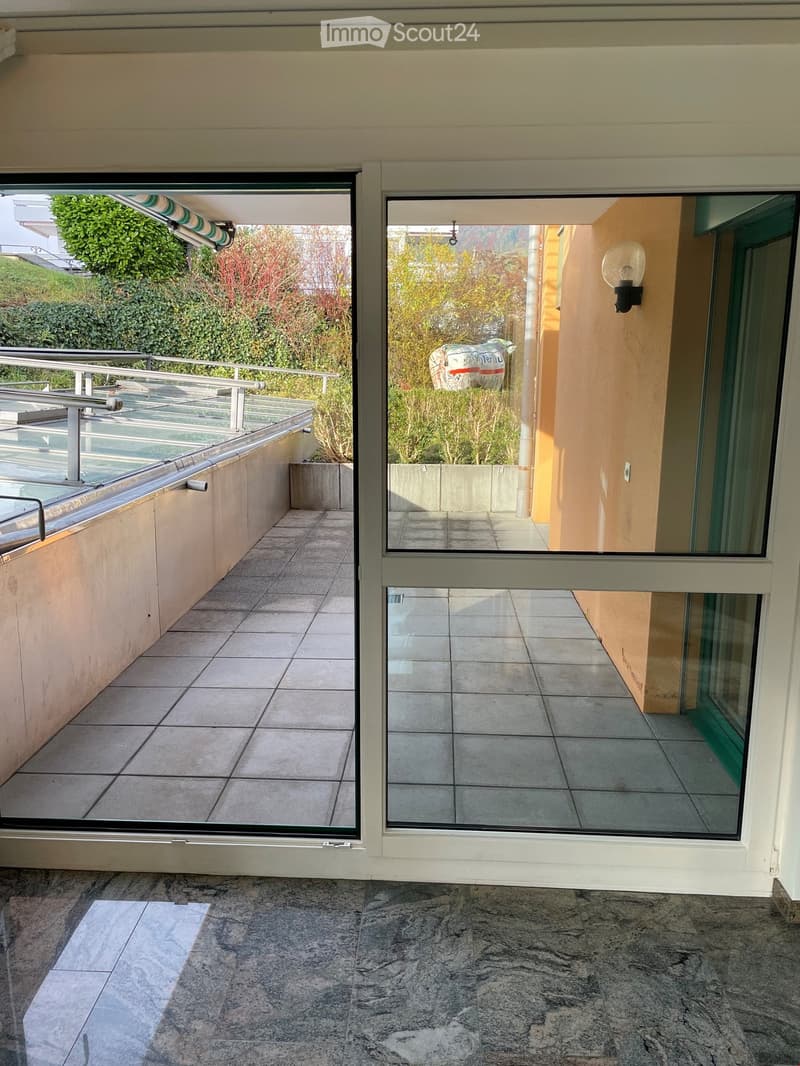 Balcony with sliding glass doors, tiled floor, metal railing, wall lamp, view of greenery