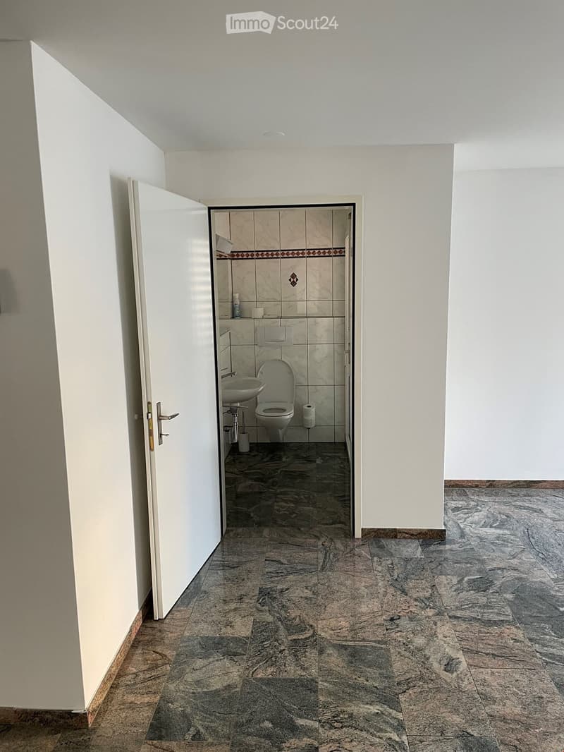 Empty bathroom with white walls, marble floor, white door, sink, toilet, and shower area
