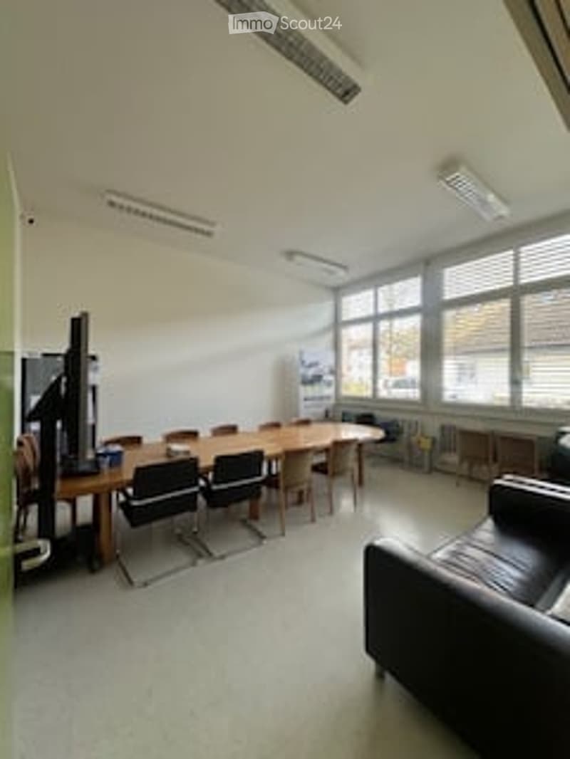 long wooden table, black chairs, black leather couch, monitor, large windows