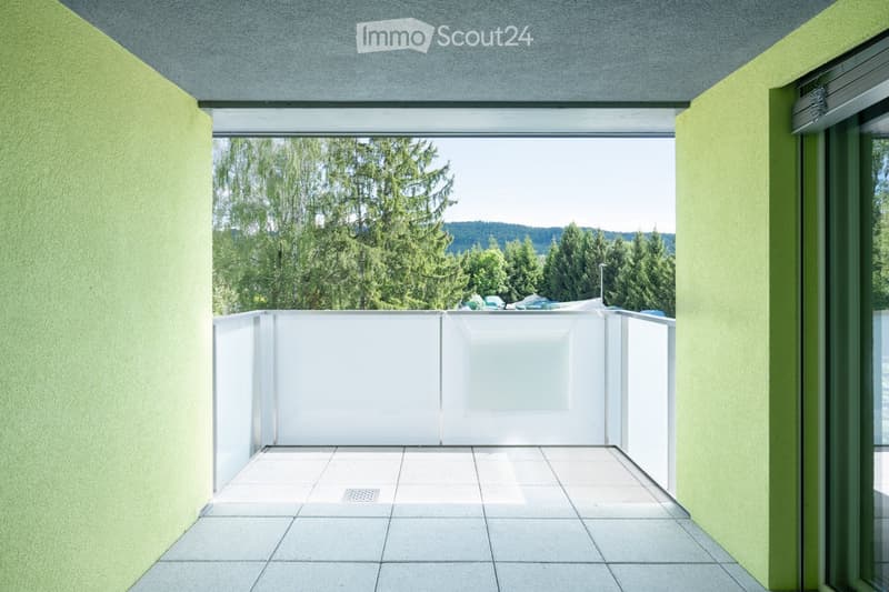 Balcony / Terrace. Modern balcony with white tiled floor, glass railing, and green walls, offering a view of trees and a distant landscape.