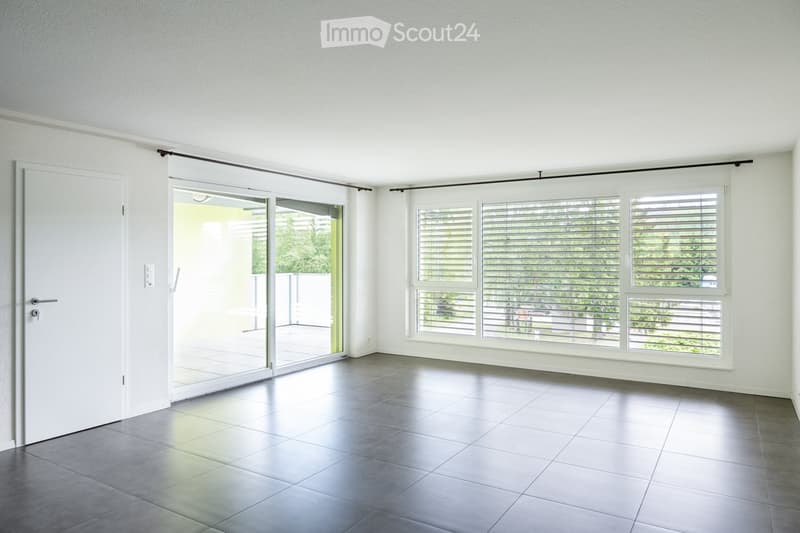 Unfurnished Room. Empty room with white walls, grey tiled floor, large windows with blinds, and a sliding glass door leading to a balcony.