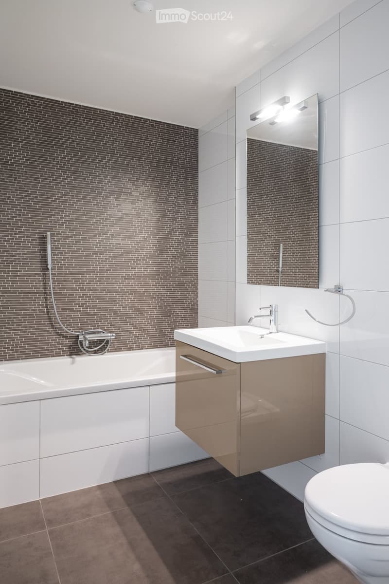 Bathroom. Modern bathroom with a bathtub, sink, toilet, and large mirror. Features dark brown tiled walls and a sleek, contemporary design.