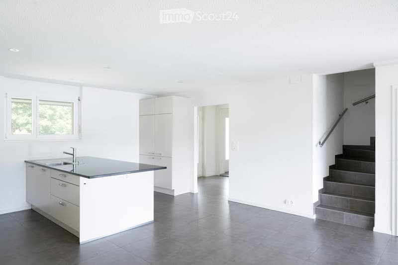 Kitchen. Modern, minimalist kitchen with white cabinets, a central island, and a sink. The space features grey tiled flooring and a staircase leading upwards.