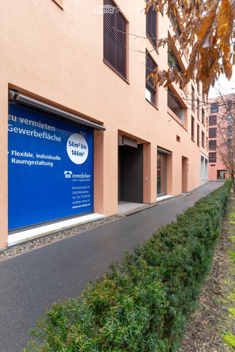 A modern apartment building with beige walls, glass windows, and a blue sign advertising flexible office spaces.