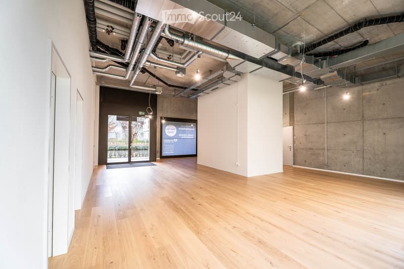 Empty room with wooden floors, white walls, large glass doors, and exposed ceiling pipes.