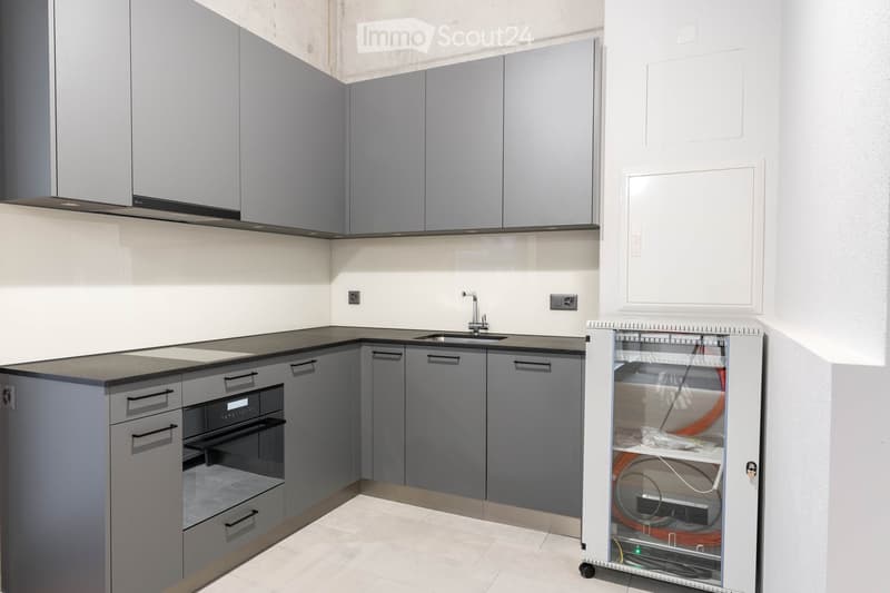modern kitchen with gray cabinets, black countertops, stainless steel sink, built-in oven, and a white electrical panel