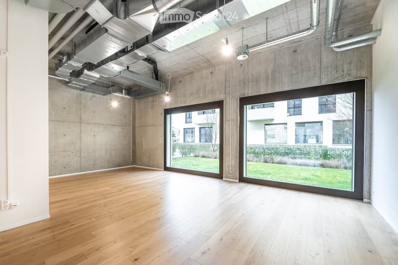 Empty room with hardwood floors, large windows, concrete walls, and ceiling with exposed pipes and lights