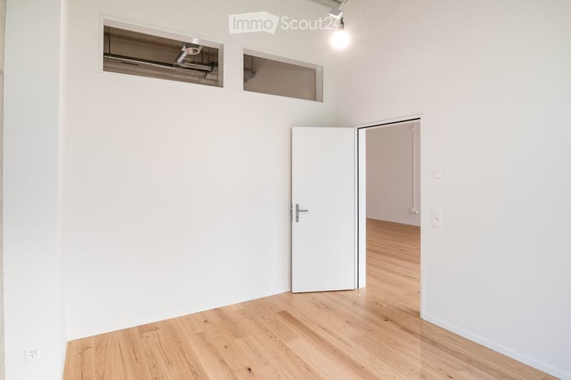 Empty room with white walls, wooden floor, two windows, and two doors.