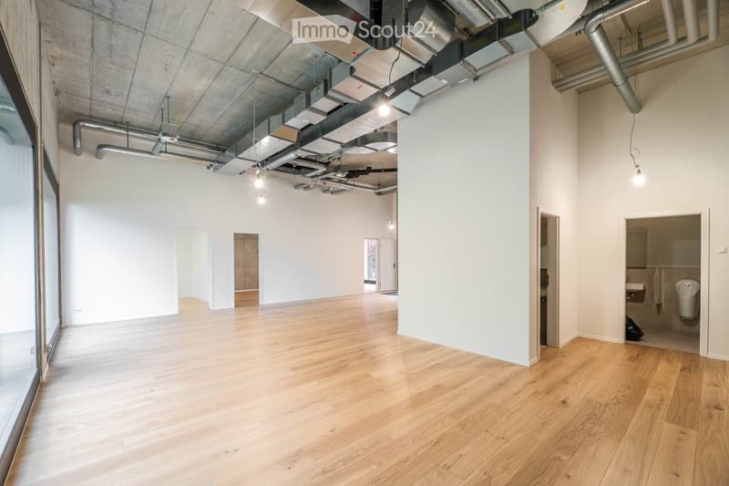 large open space, hardwood floors, white walls, exposed ceiling ducts, large windows