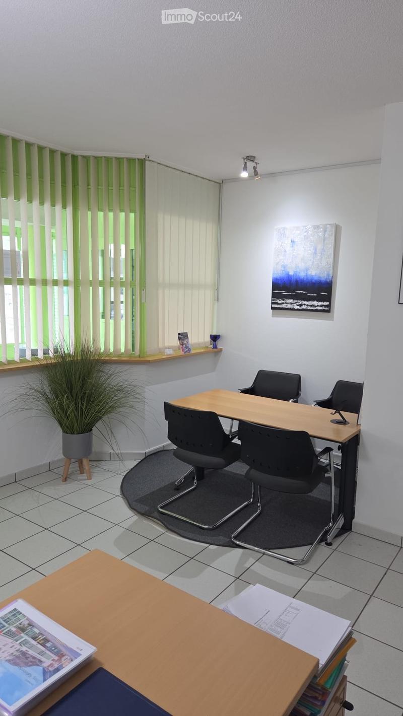 Office room with a desk, chairs, table, plant, and artwork on the wall.